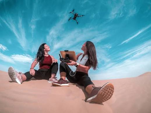 two-girls-on-beach-looking-at-drone-above